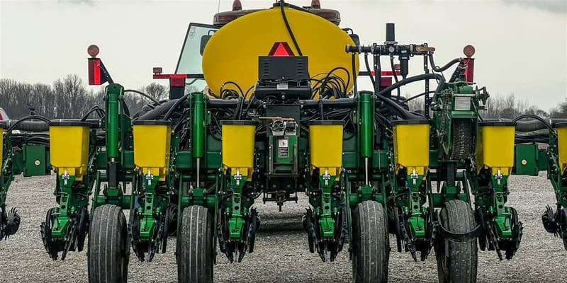 Rear view of a green John Deere planter with yellow tanks on a gravel lot